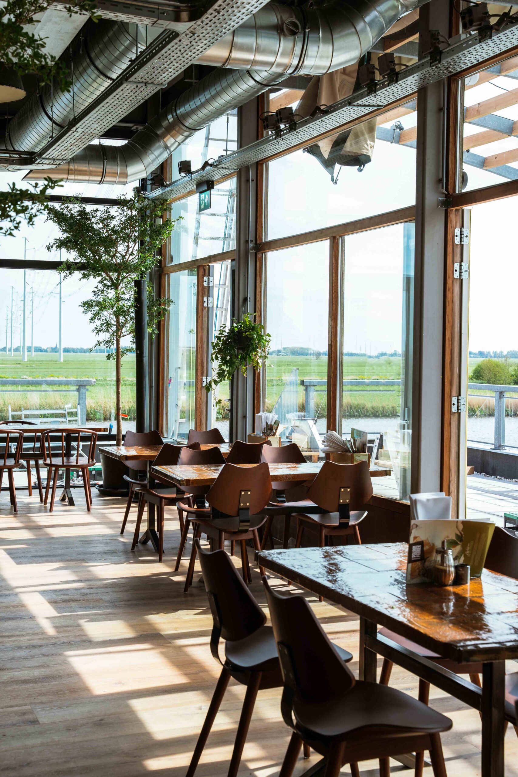Zaal met houten tafels en grote ramen op de polder bij Brasserie Polderfabriek