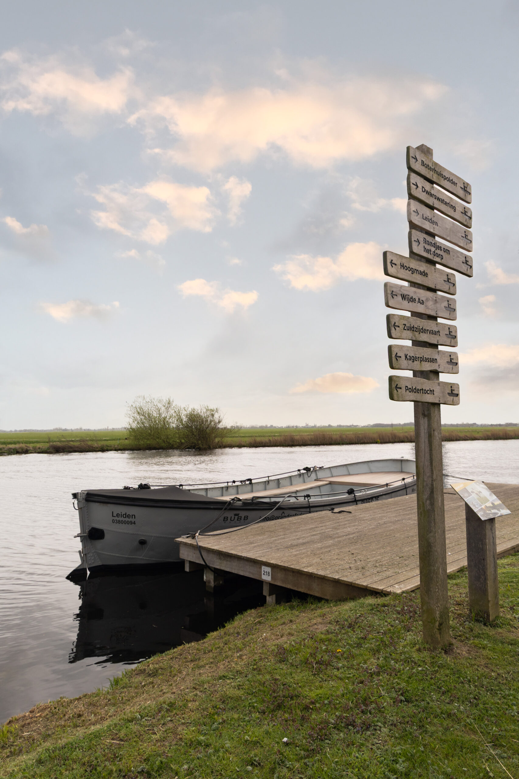 Sloep aan de aanlegsteiger met een wegwijzer bij Brasserie Polderfabriek in de polder